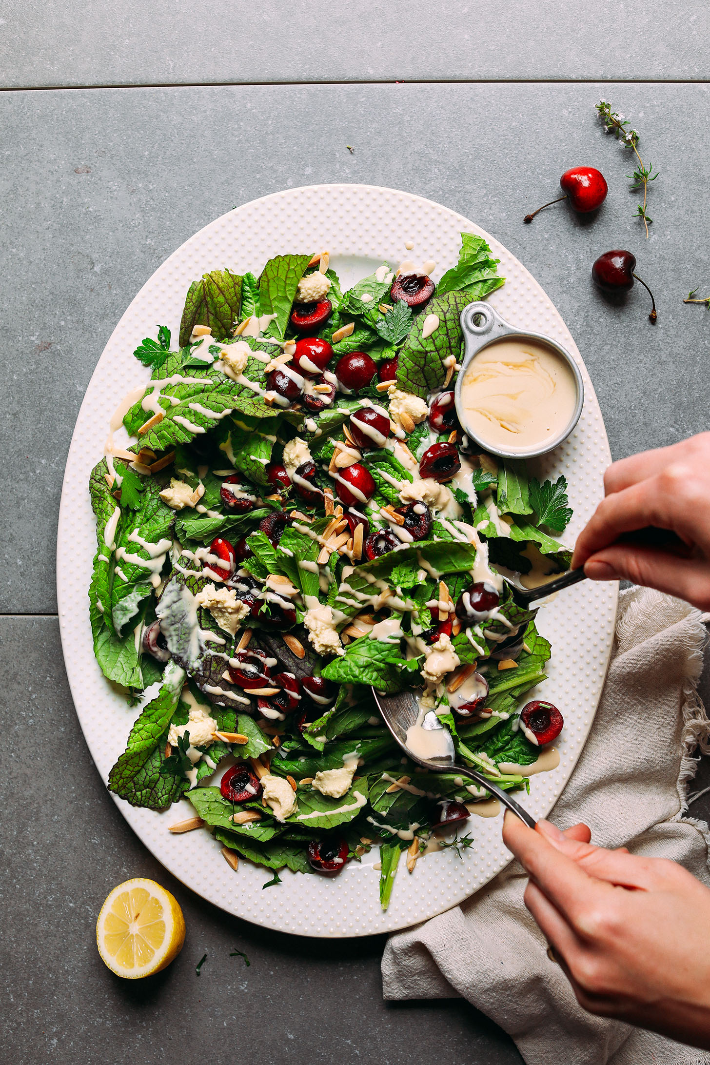 Large ceramic platter filled with Mustard Green Salad with Cherries, Toasted Almonds, Nut Cheese, and Tahini Dressing