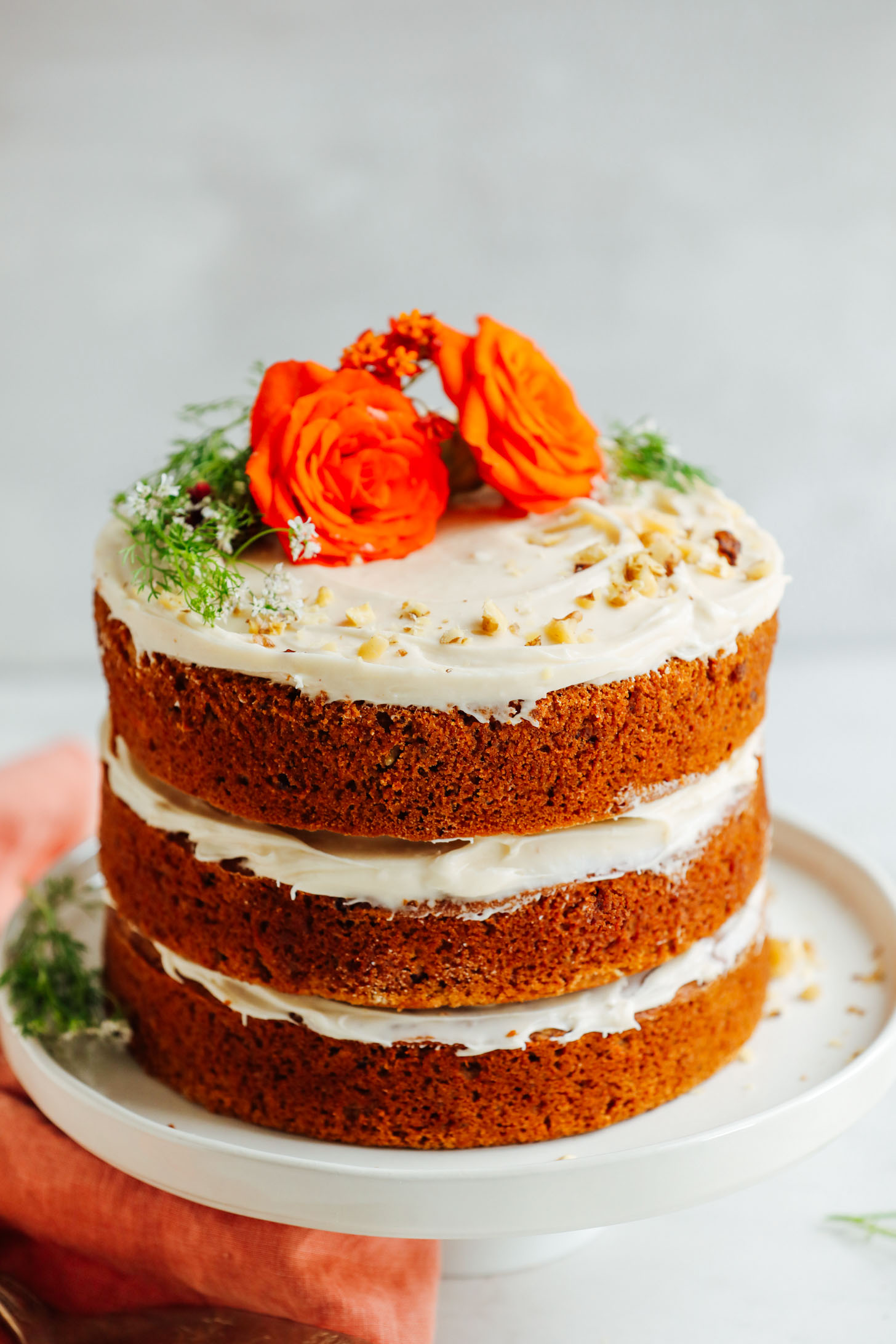 Three-layer Vegan Gluten-Free Carrot Cake decorated with flowers and chopped nuts