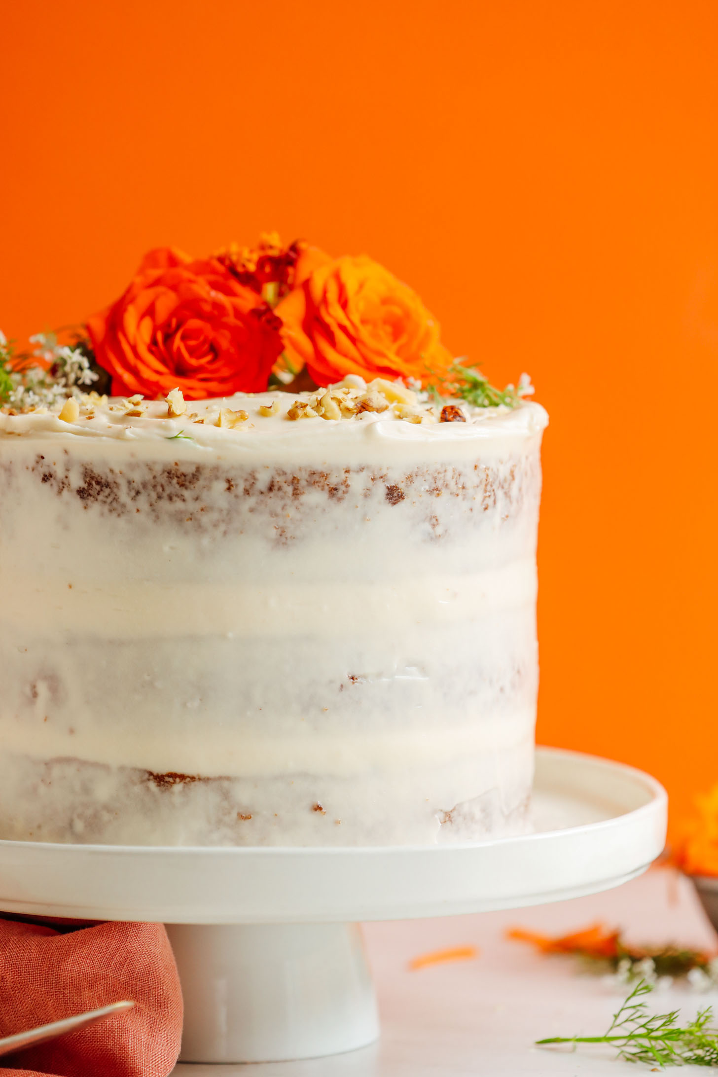 Lightly frosted Vegan Gluten-Free Carrot Cake decorated with fresh flowers and chopped nuts