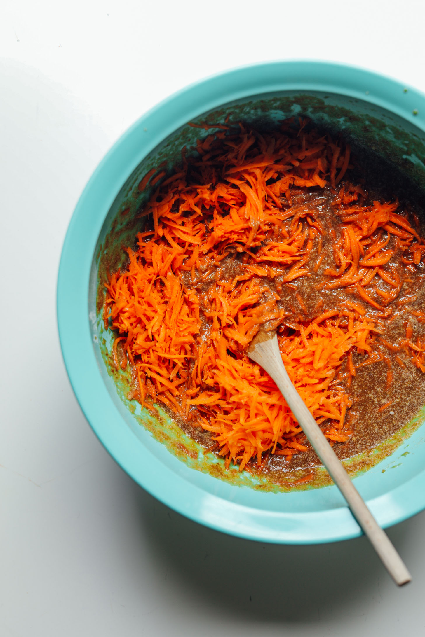 Stirring shredded carrots into a mixing bowl filled with gluten-free vegan carrot cake batter