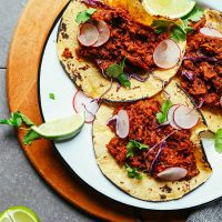 Plate with three Vegan Barbacoa Tacos topped with sliced cabbage, radishes, cilantro, and lime