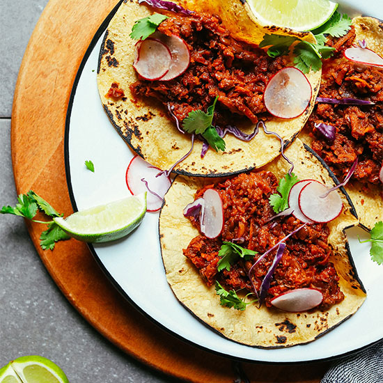 Plate with three Vegan Barbacoa Tacos topped with sliced cabbage, radishes, cilantro, and lime