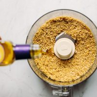 Drizzling olive oil into a food processor to make Vegan Brazil Nut Parmesan Cheese