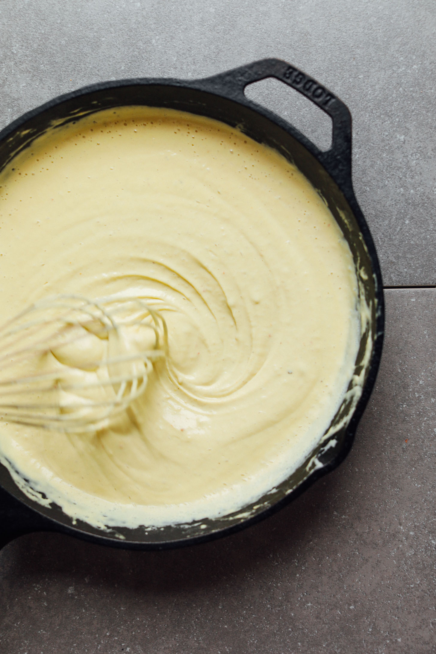 Whisking vegan cheese sauce ingredients in a cast iron skillet
