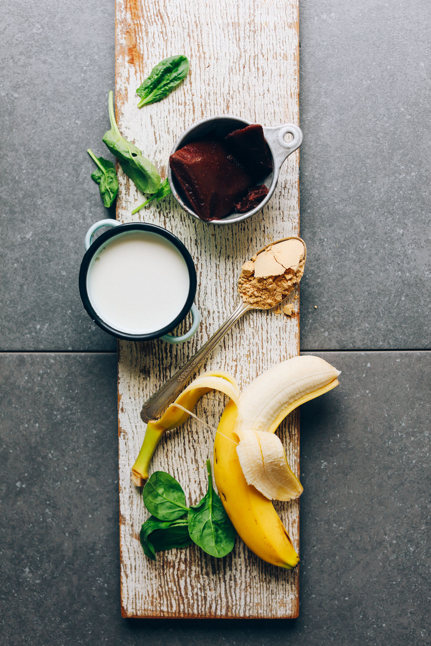 Wood plank with banana, peanut butter powder, nut milk, spinach, and acai for making Peanut Butter & Jelly Acai Bowls