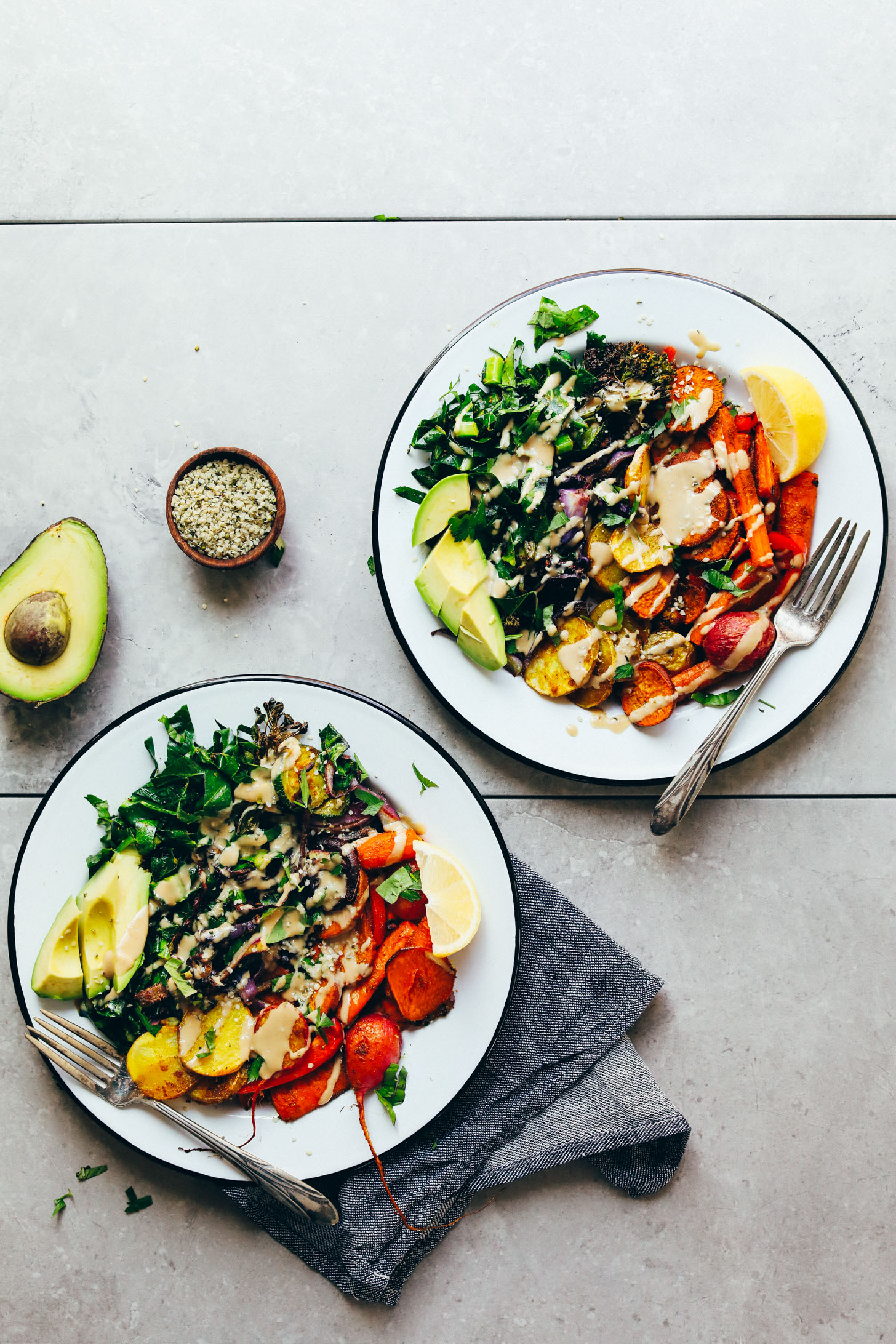 Two big dinner bowls full of Roasted Rainbow Vegetables, avocado, hemp seeds, and tahini dressing