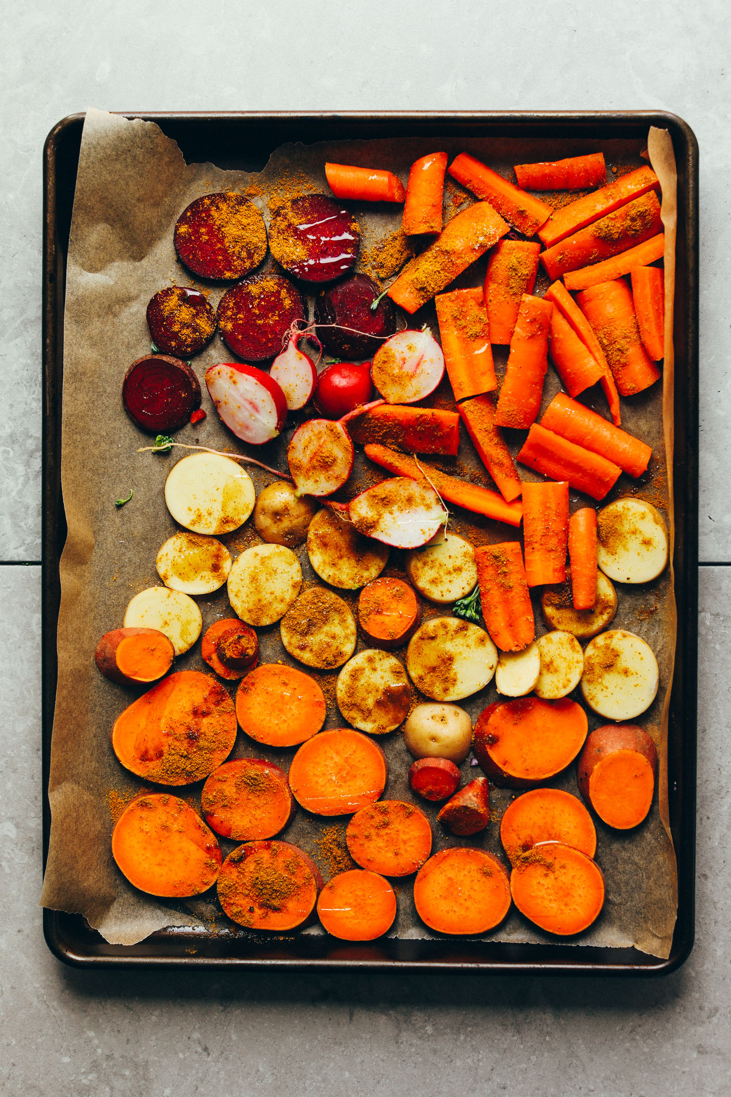 Parchment-lined baking sheet filled with carrots, beets, radish, and sweet potato for roasting
