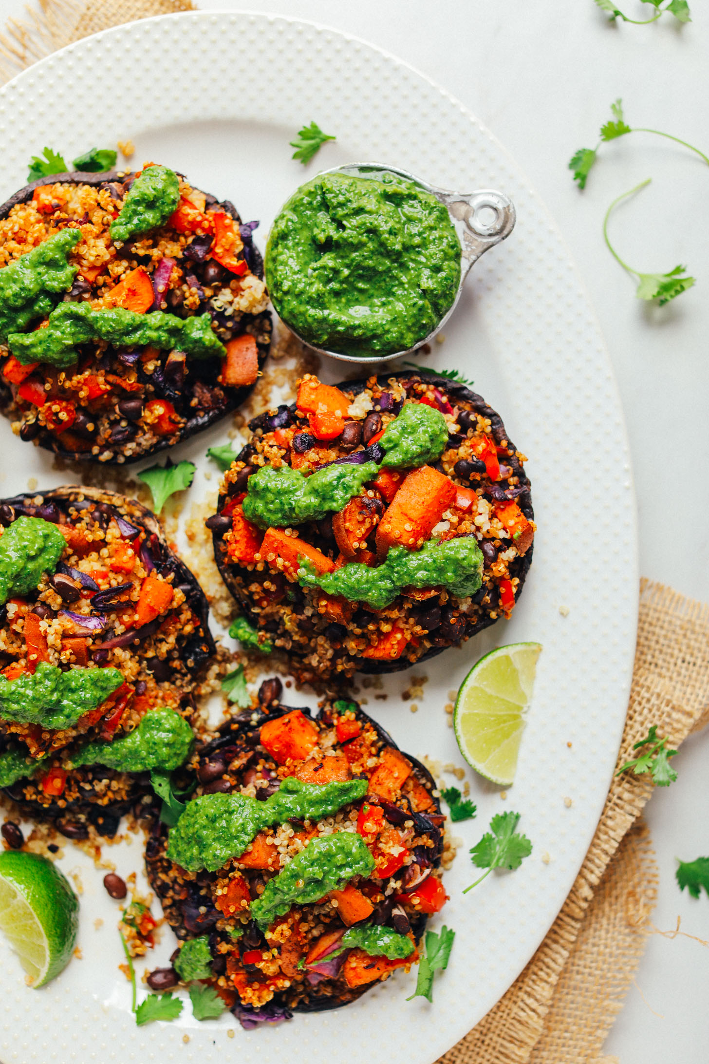 Ceramic serving platter with four Vegetable Quinoa Stuffed Portobello Mushrooms and a side of chimichurri