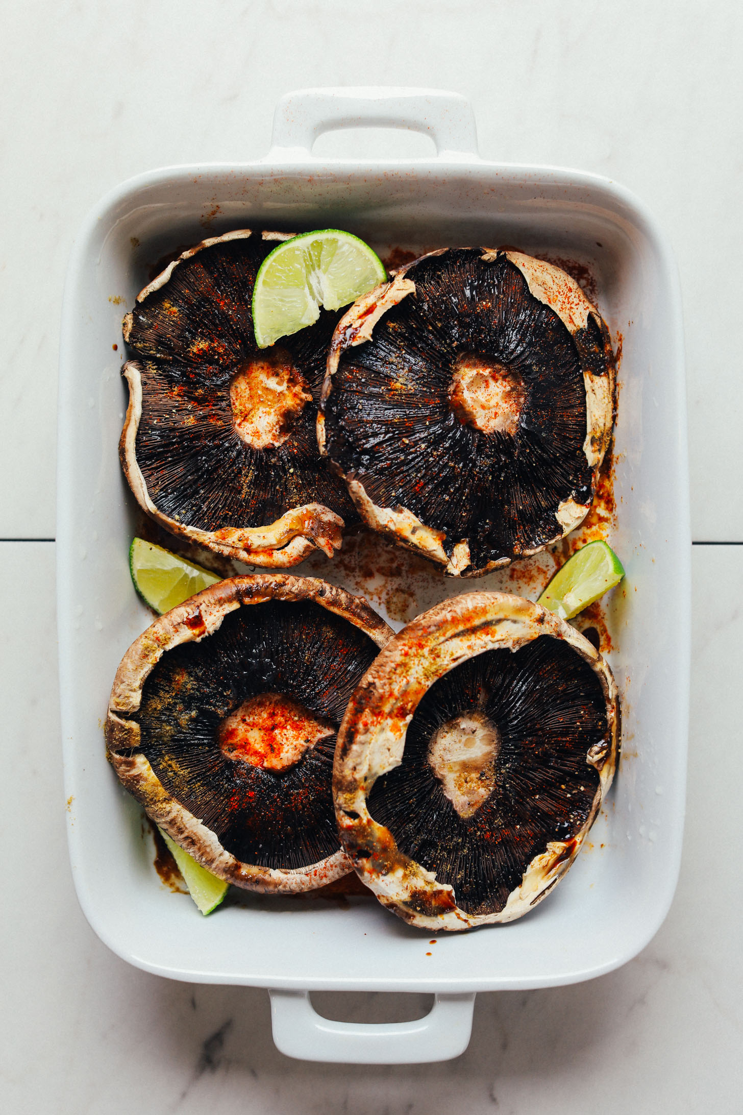 Ceramic baking dish with four portobello mushrooms, spices, and fresh lime wedges