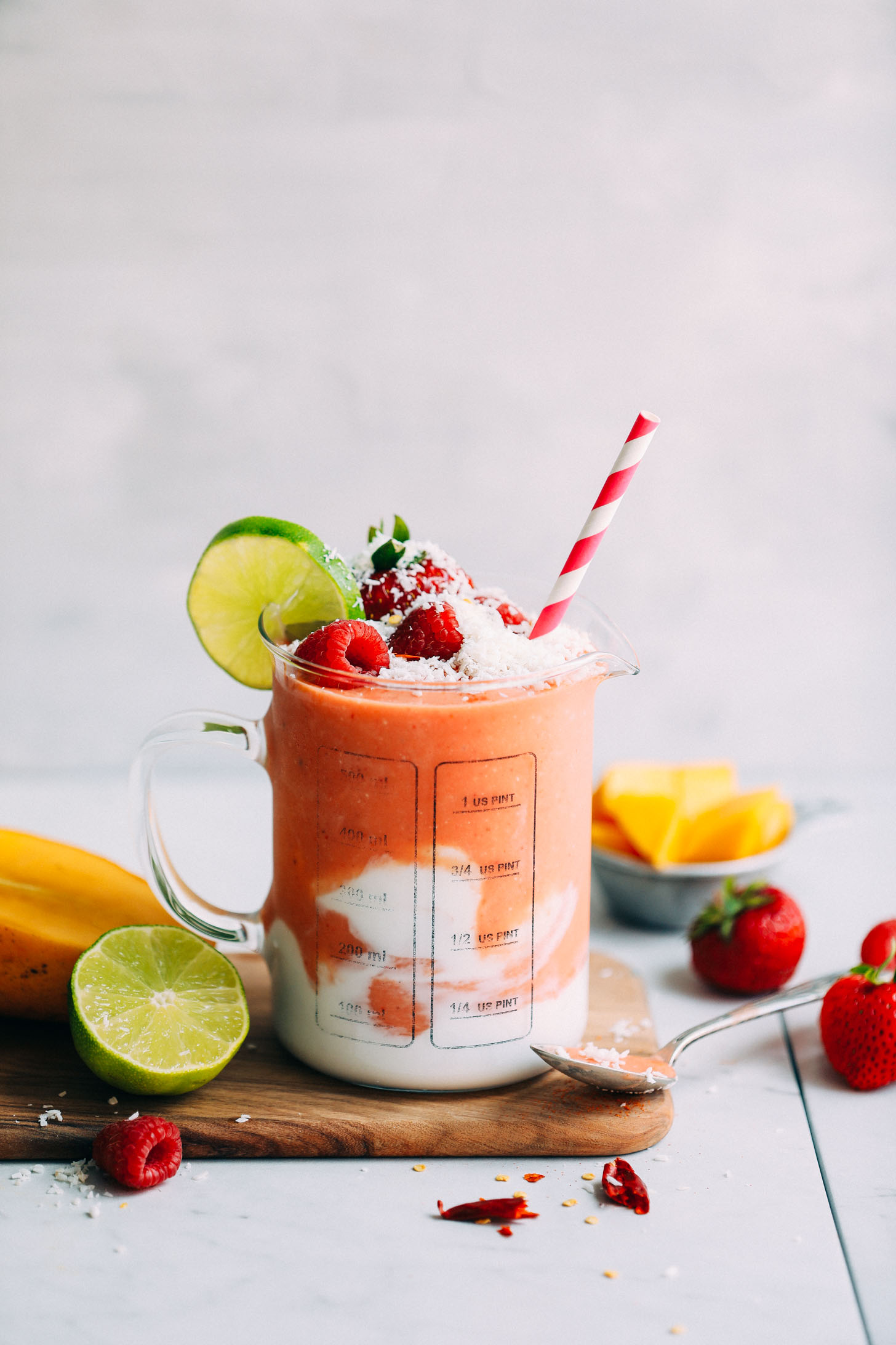 Glass serving jar with a swirl of coconut milk and filled with Gingery Mango & Berry Smoothie