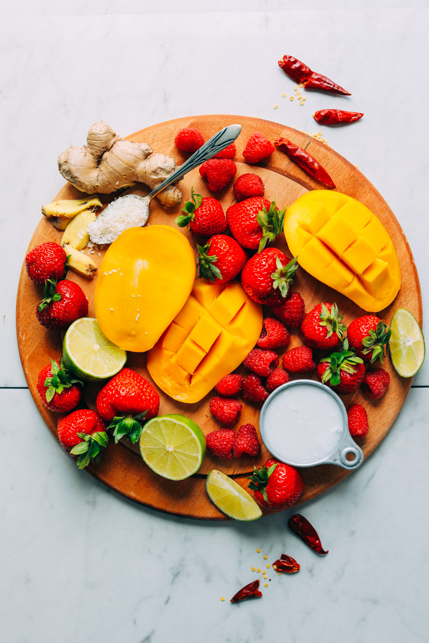 Wood cutting board with fresh fruit for making a vegan Gingery Mango & Berry Smoothie
