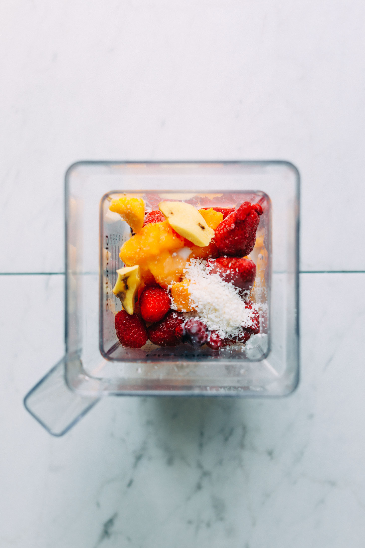 Fresh fruit, ginger, and shredded coconut in a blender for making Gingery Mango & Berry Smothie