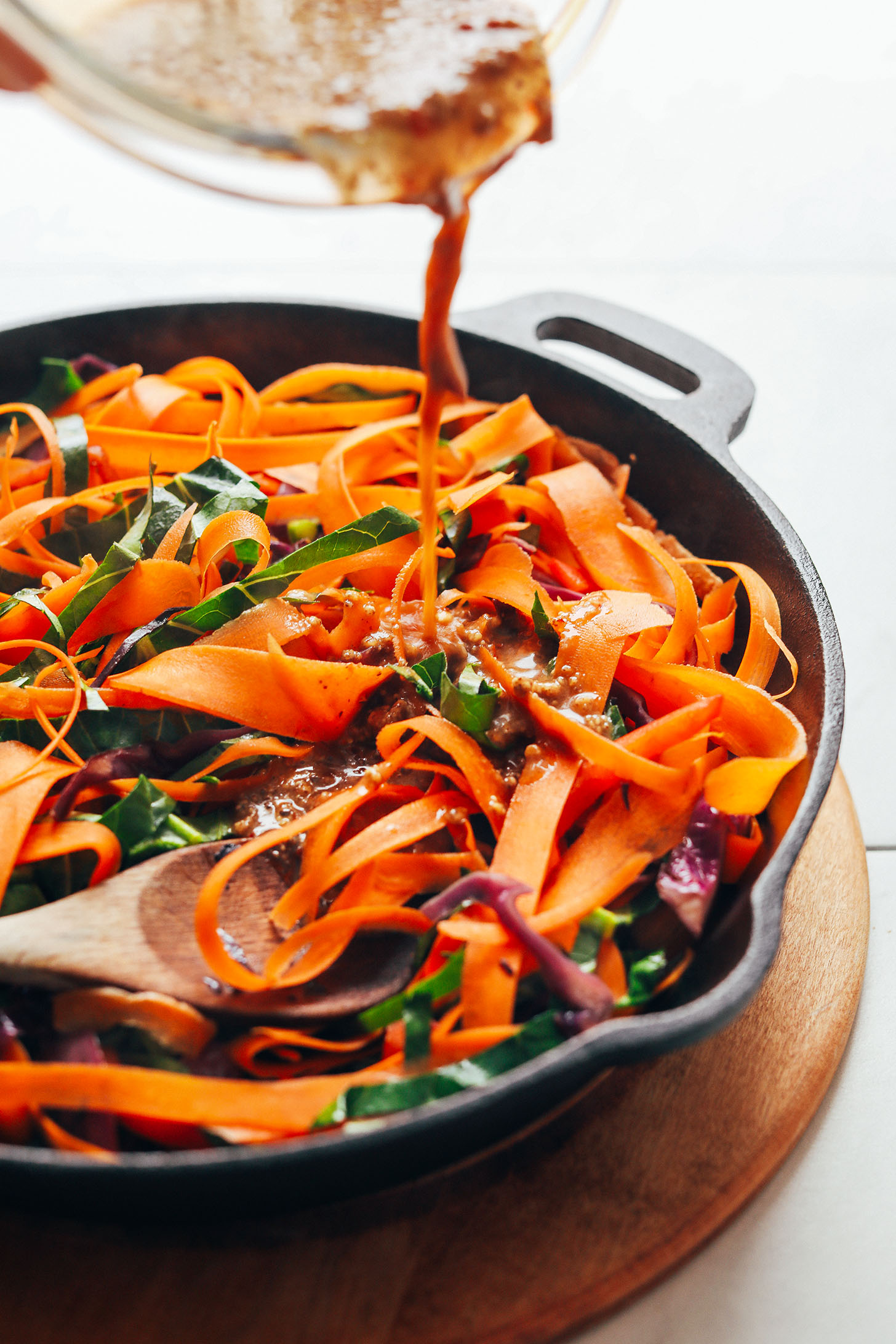Pouring sauce onto a cast iron skillet filled with Noodle-Free Pad Thai