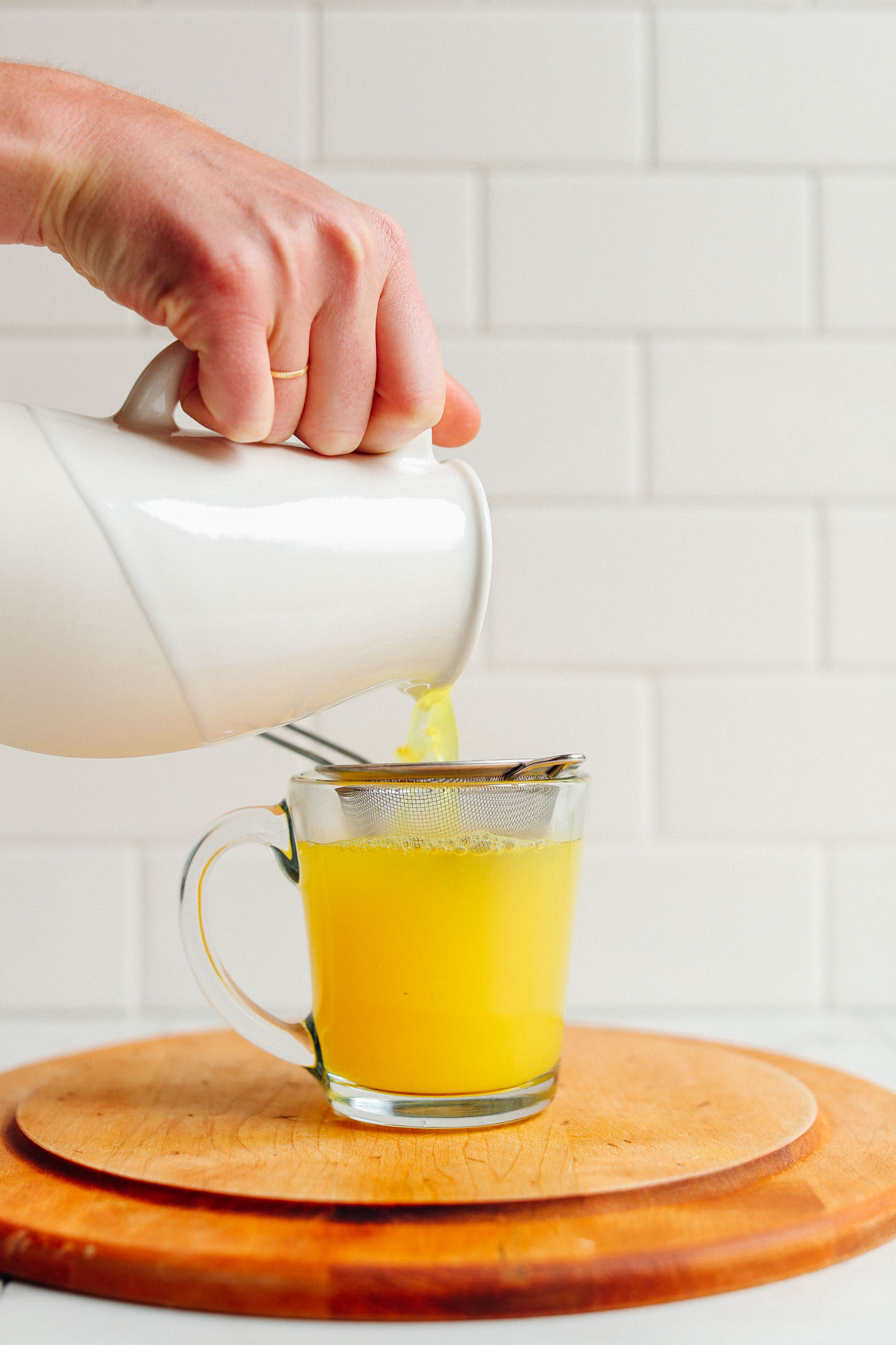 Pouring Turmeric Ginger TONIC through a strainer into a glass mug