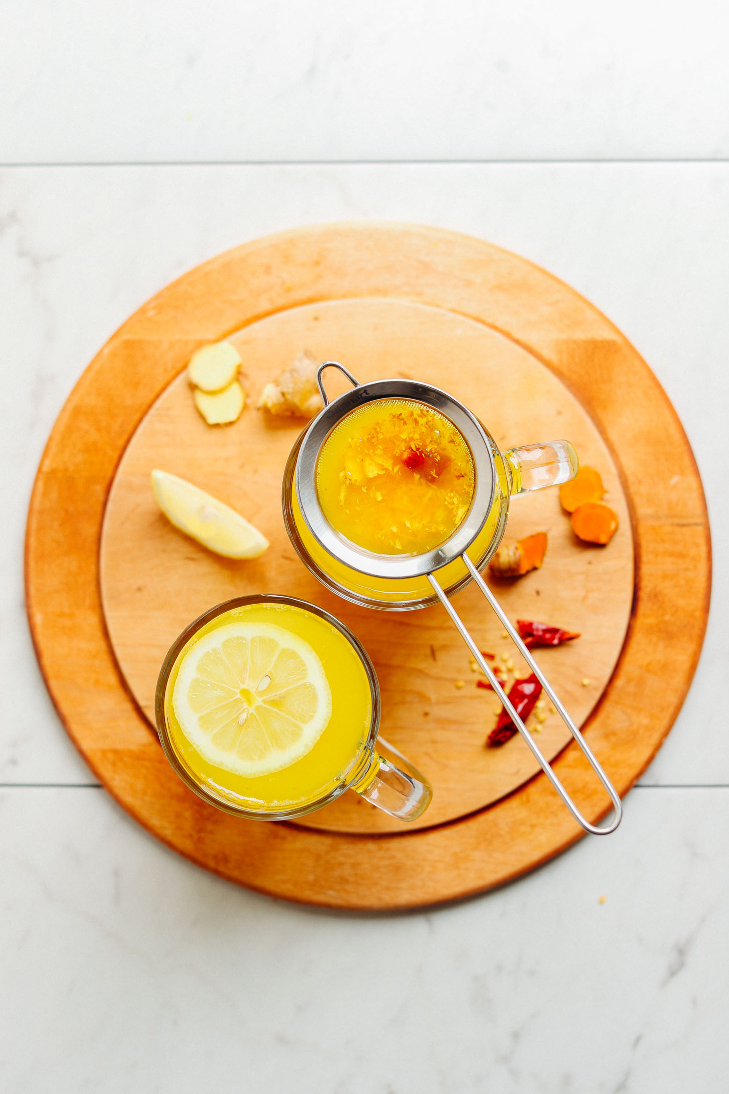 Wood cutting board with two glass mugs full of Turmeric Ginger TONIC