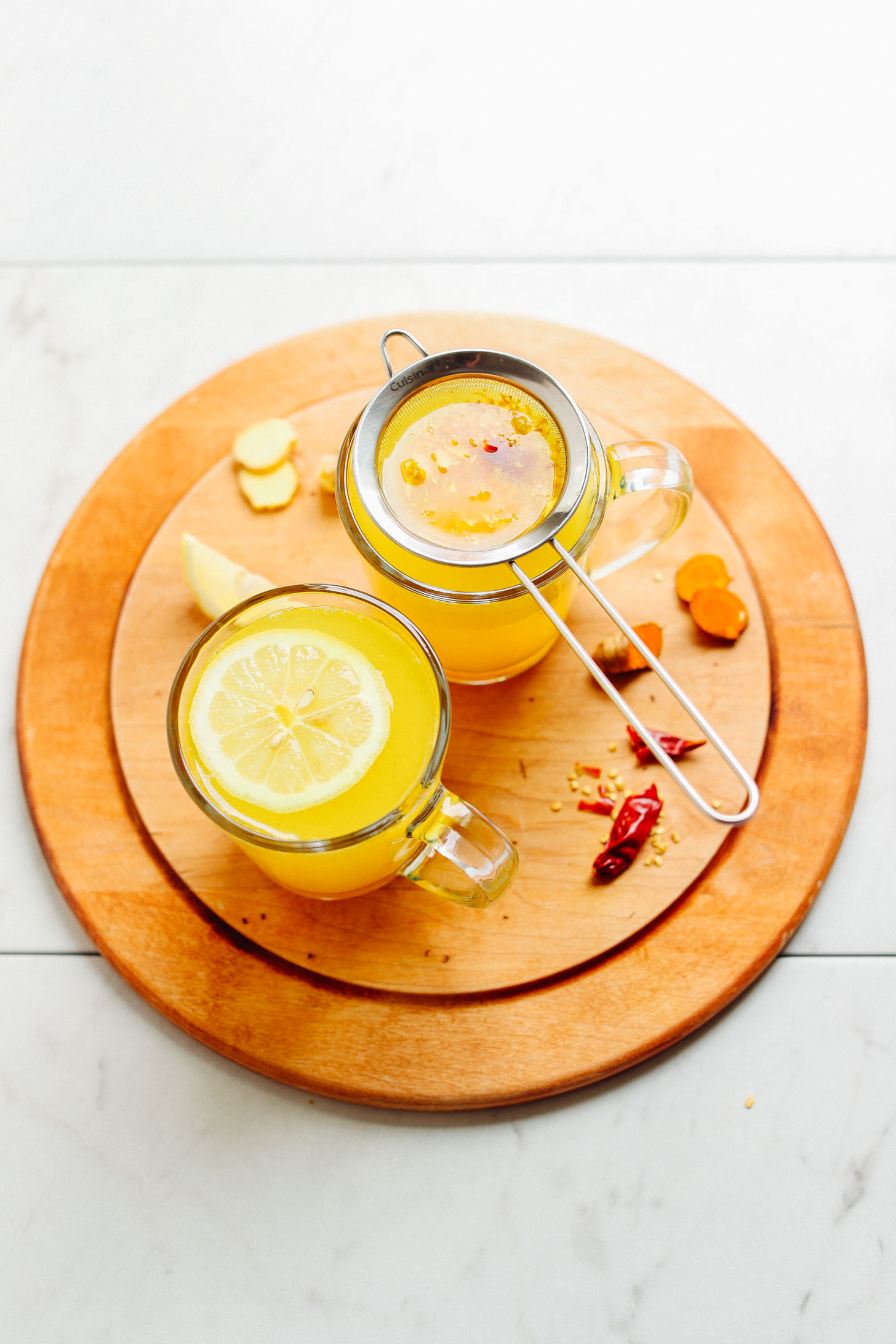 Mugs of healing Turmeric Ginger TONIC displayed on a cutting board with ingredients