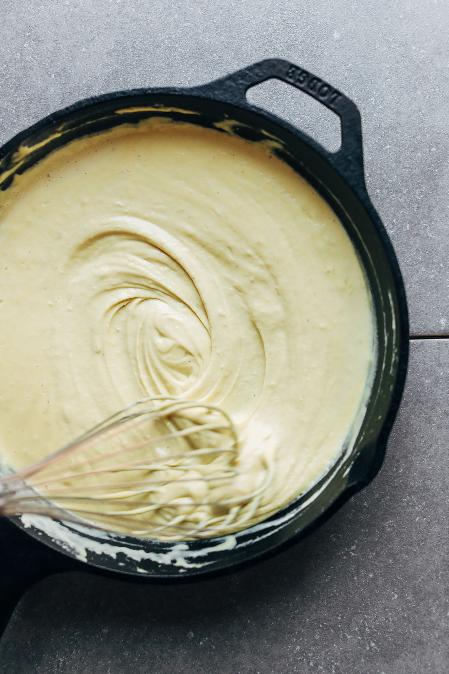Whisking vegan alfredo sauce in a cast iron skillet