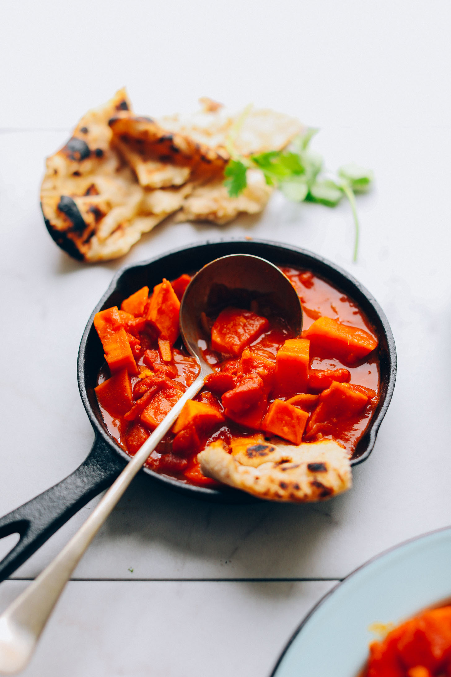 A cast iron skillet filled with 30-Minute Sweet Potato Cauliflower Curry and a ladle for serving