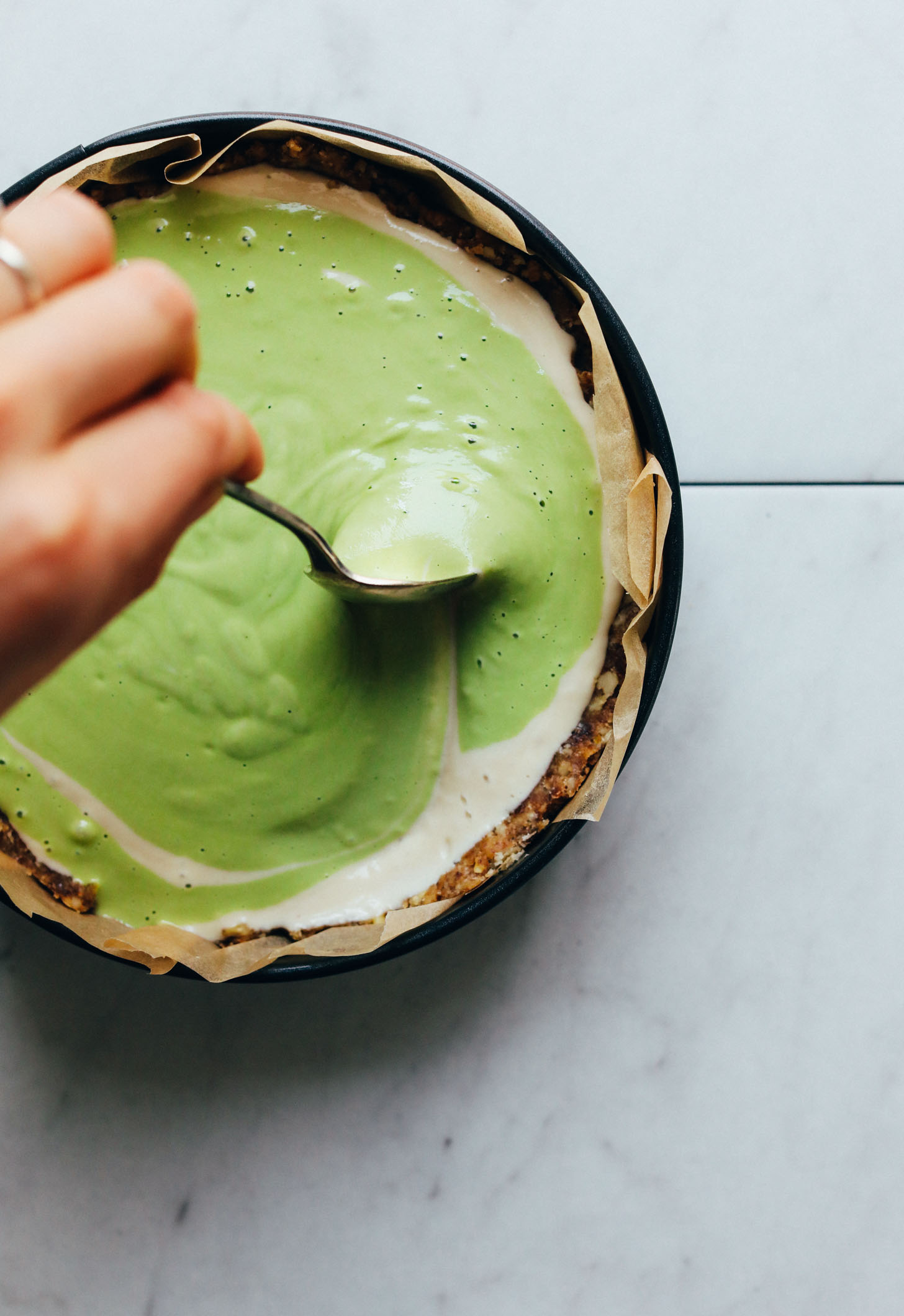 Using a spoon to make a swirl pattern for gluten-free vegan Matcha Swirl Cheesecake