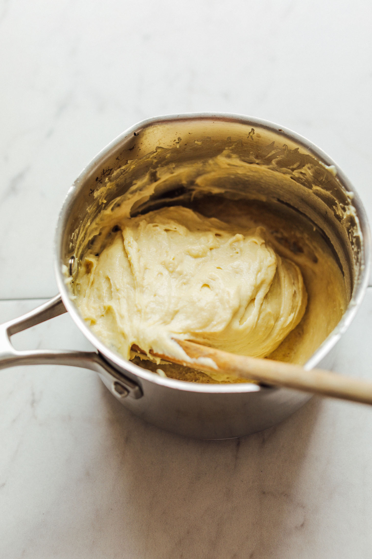 Using a wooden spoon to stir a saucepan of amazing Vegan Mozzarella Cheese