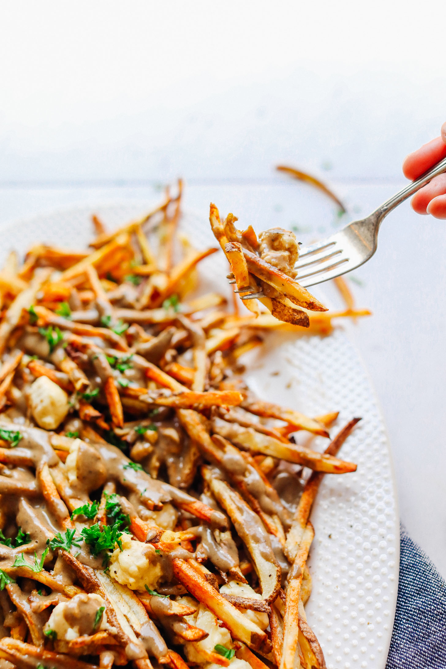 Using a fork to grab a bite of Vegan Poutine made from crispy baked fries, mushroom gravy, and vegan cheese curds