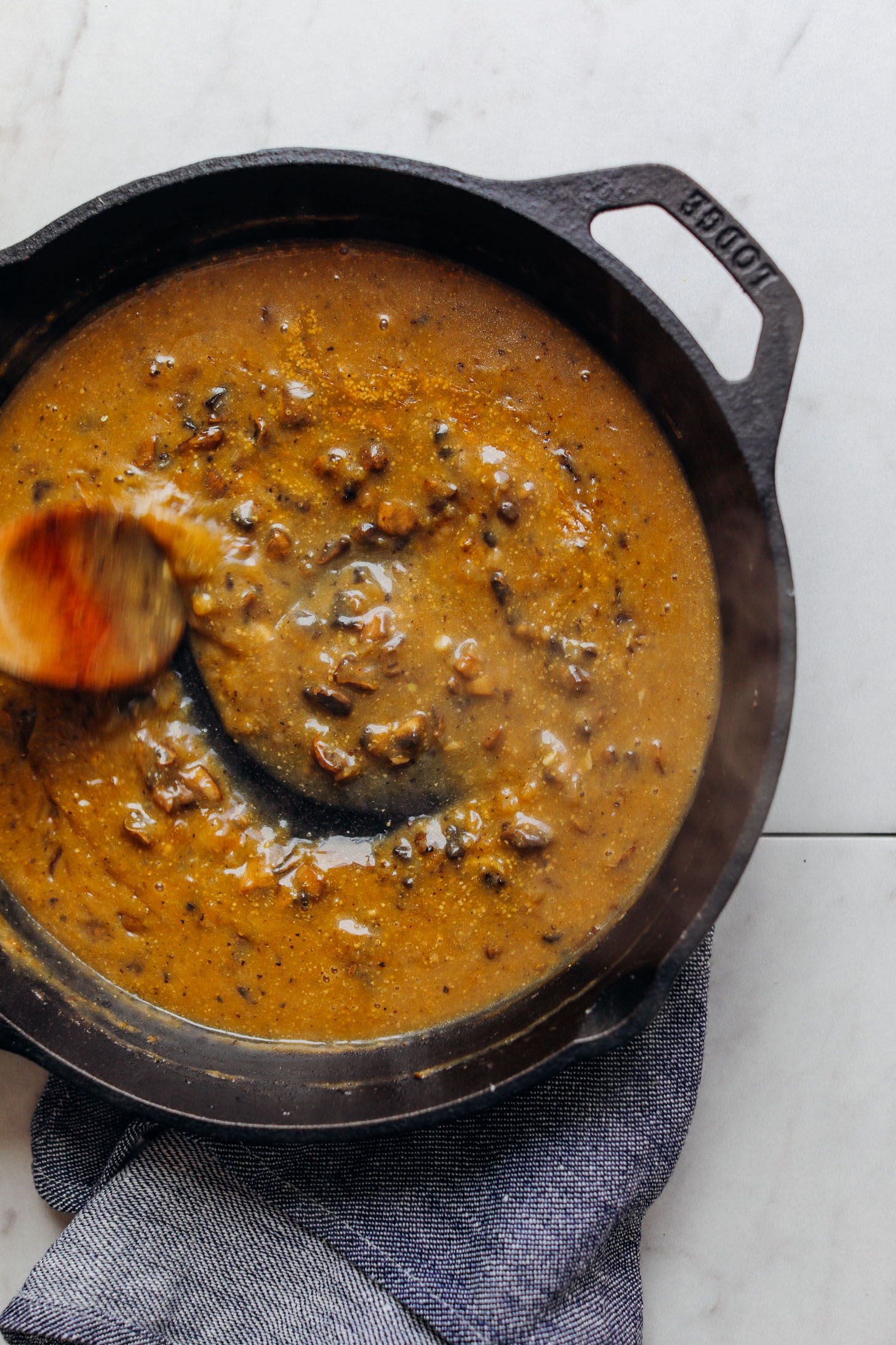 Using a wooden spoon to stir mushroom gravy in a cast iron skillet