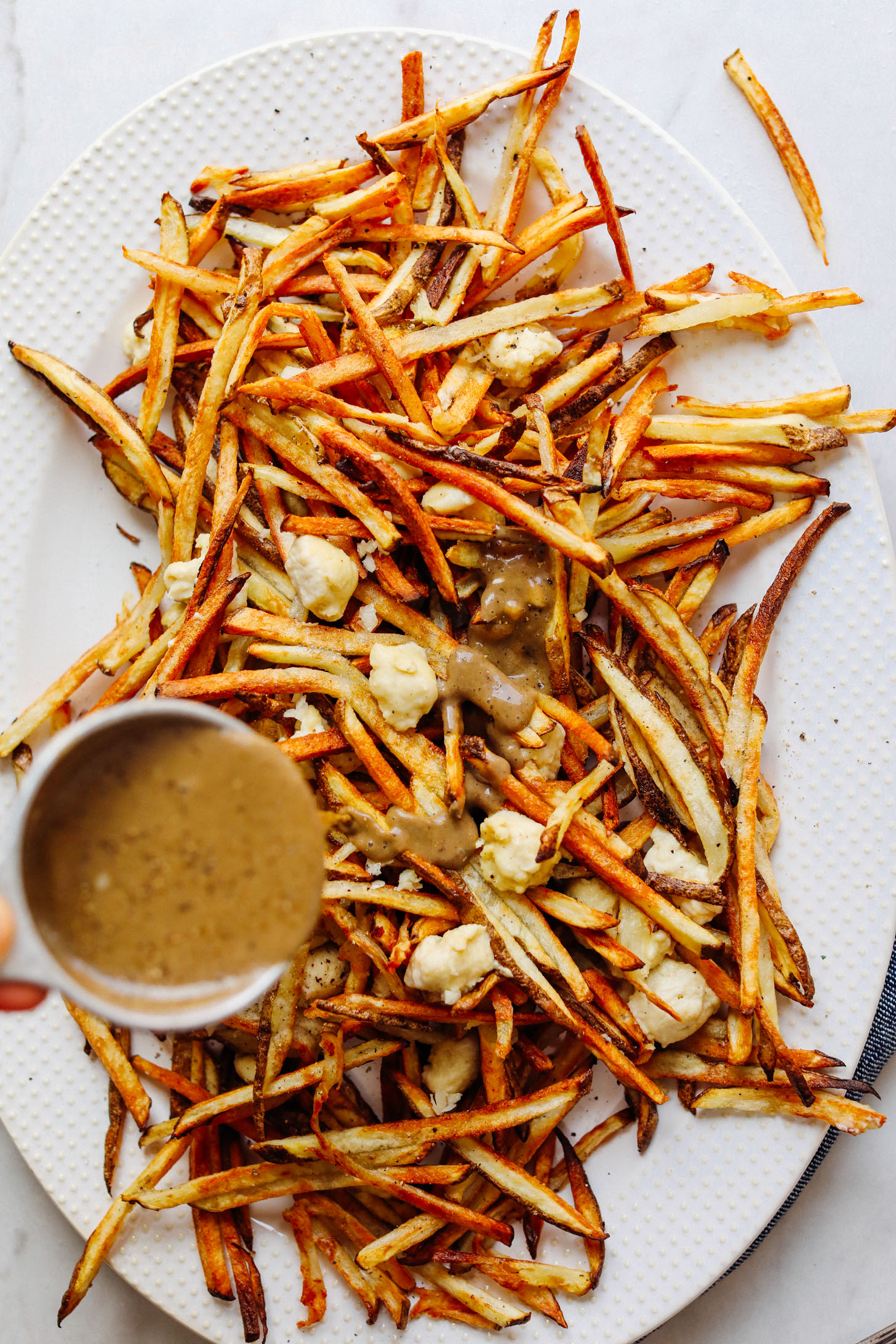 Pouring vegan mushroom gravy over crispy baked fries for Vegan Poutine