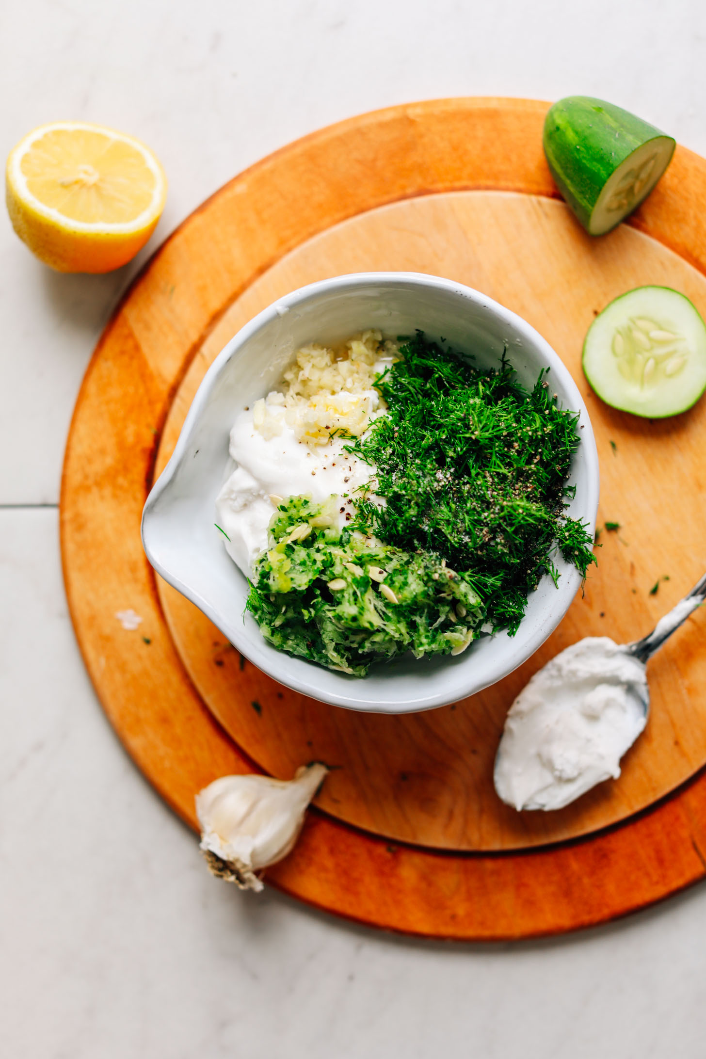 Wood cutting board with a bowl full of chopped ingredients for making Vegan Tzatziki