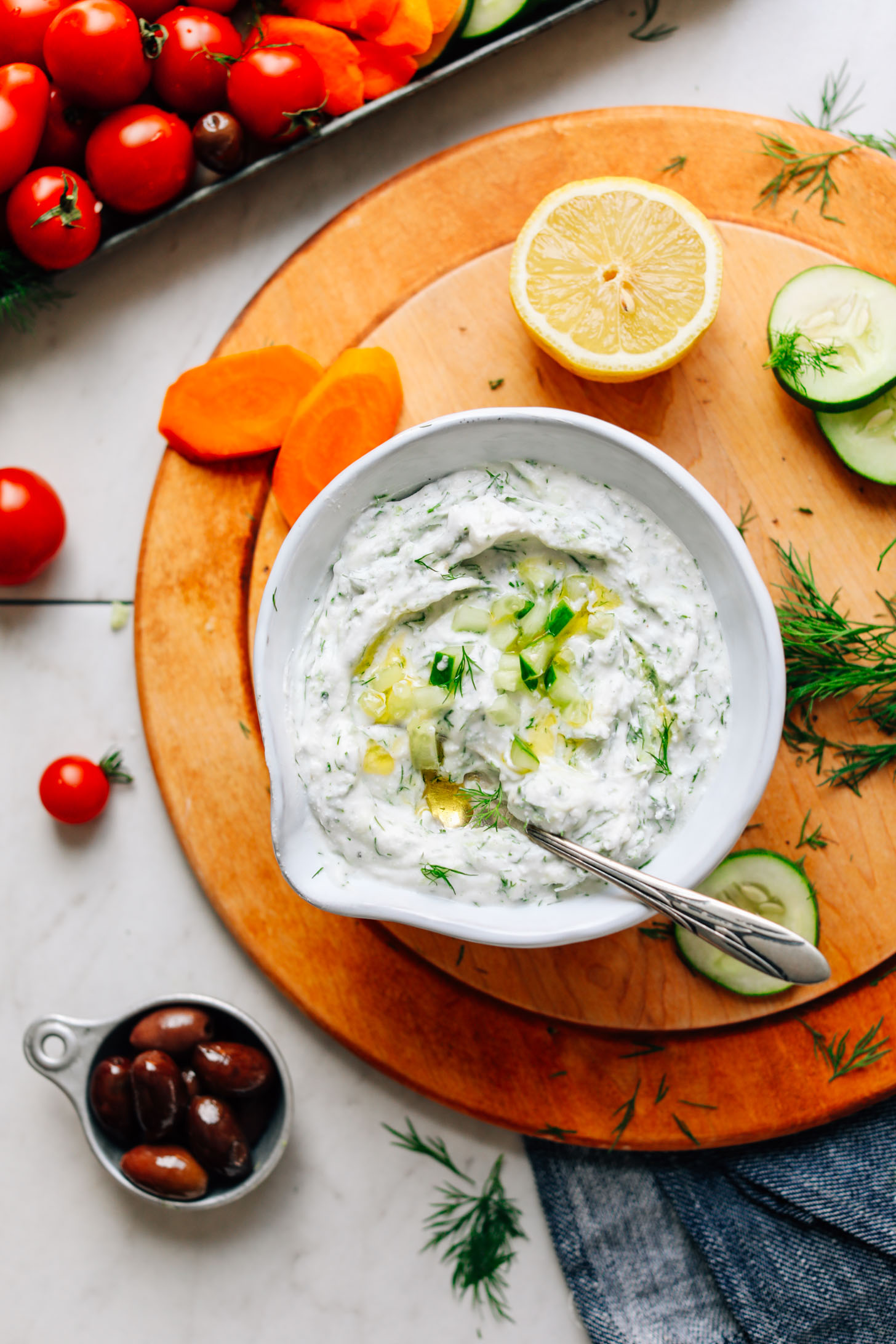 Bowl of gluten-free Vegan Tzatziki on a wood cutting board with veggies for dipping