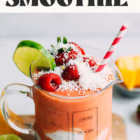 A measuring glass of our banana-free Gingery Mango Berry Smoothie recipe topped with fresh fruit and coconut