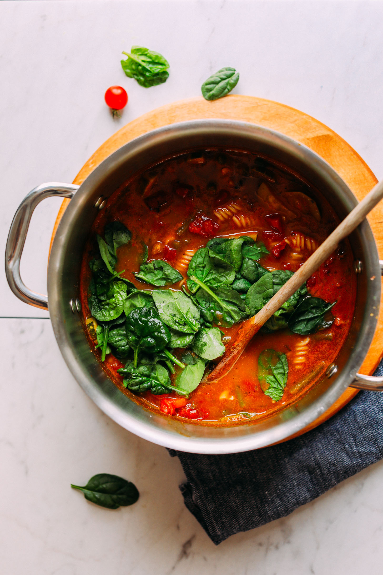 Stirring spinach into a soup pot full of gluten-free Minestrone for a healthy plant-based dinner