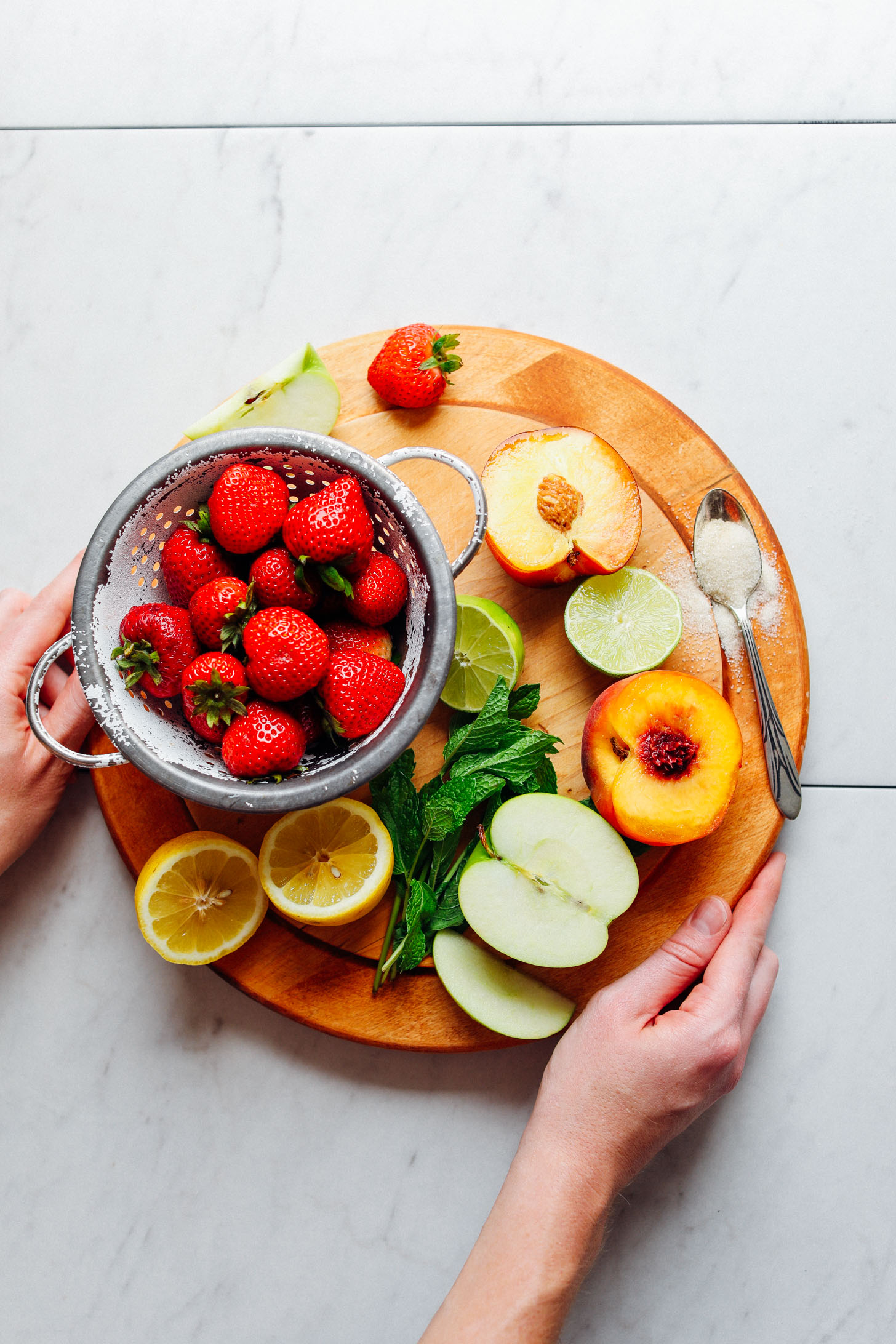 Wood cutting board displaying mint, apple, peach, lime, strawberries, and lemon