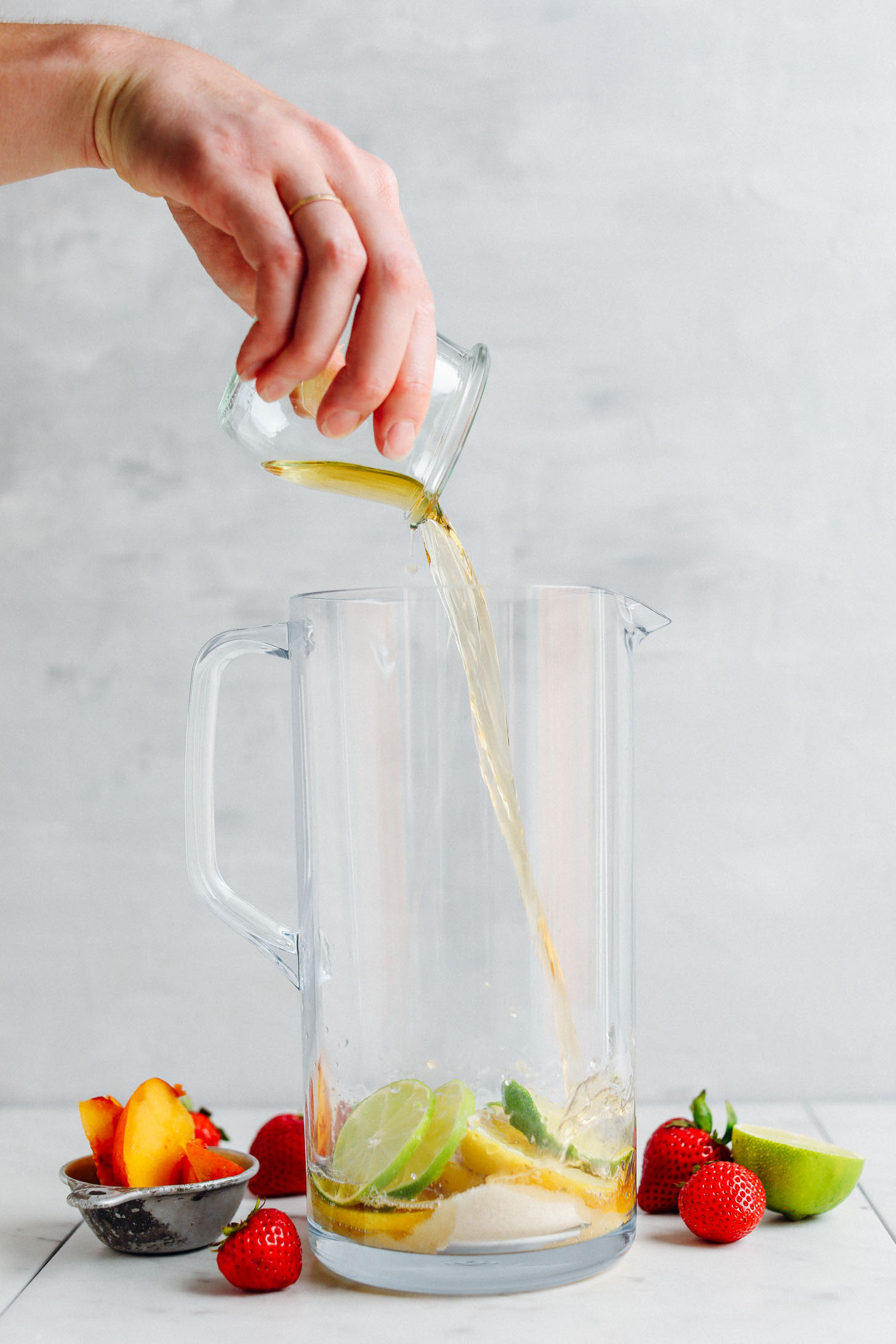 Pouring apple brandy into a pitcher with fresh lemons, limes, and sugar