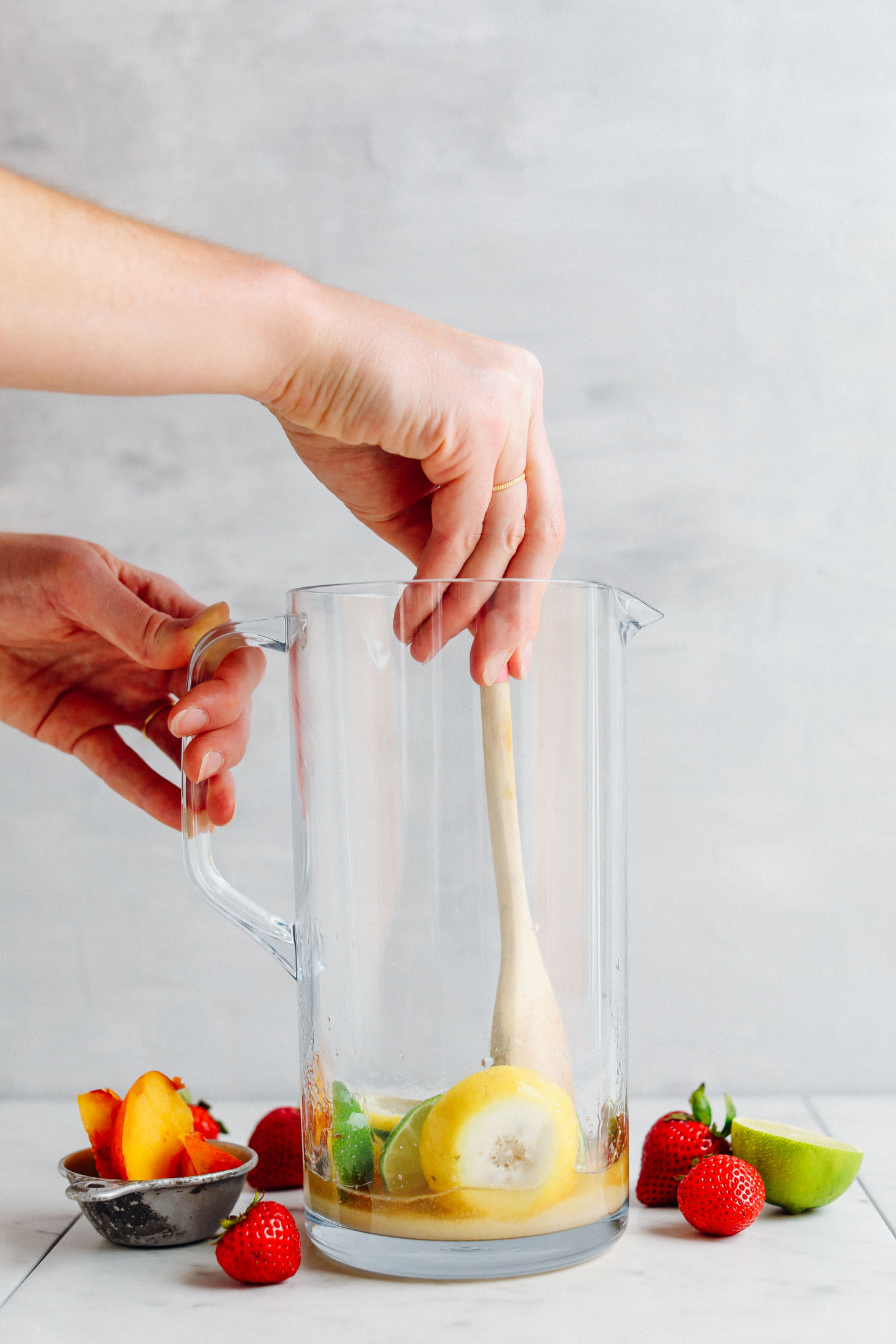 Swirling a wooden spoon in a pitcher to muddle sugar, fresh citrus and brandy