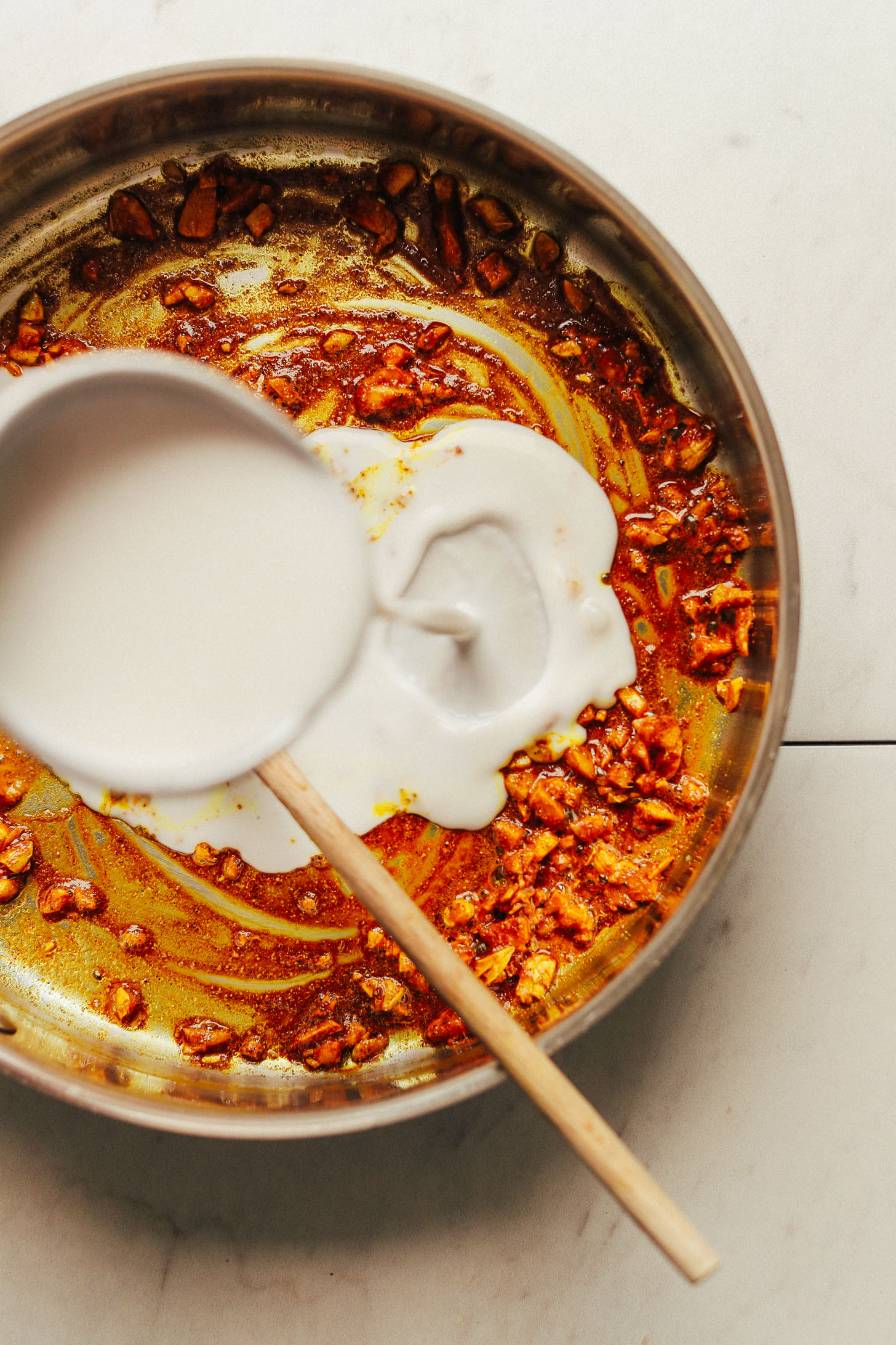 Pouring coconut milk into a pan of spices for Coconut Curried Golden Lentils