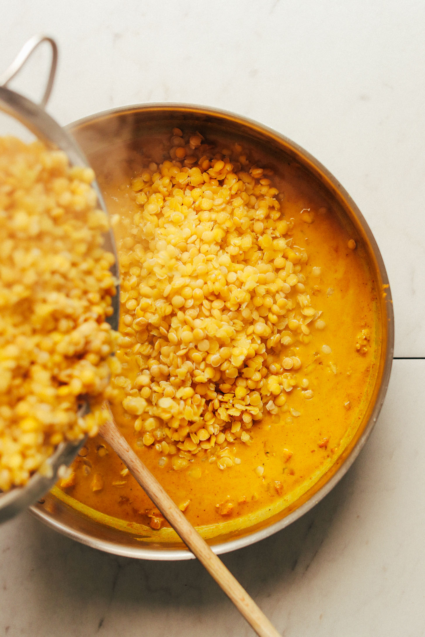Pouring strained lentils into a large pan for Coconut Curried Golden Lentils