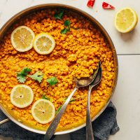 Pan of Curried Golden Lentils with two spoons, lemon slices, and cilantro
