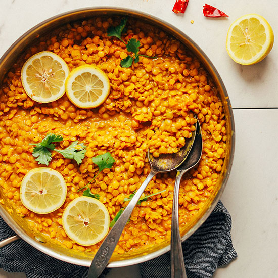 Pan of Curried Golden Lentils with two spoons, lemon slices, and cilantro