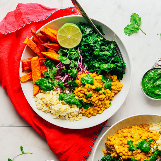 Bowls of Coconut Curried Golden Lentils with cauliflower rice, cabbage, kale, cilantro, roasted sweet potato, lime and chimichurri