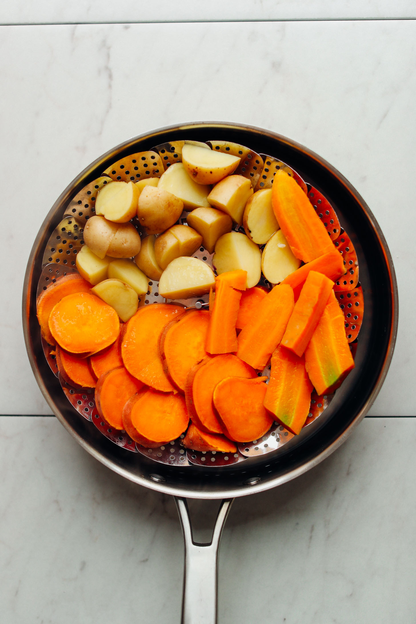 Steam basket filled with chopped potatoes, sweet potatoes, and carrots ready to be softened before roasting