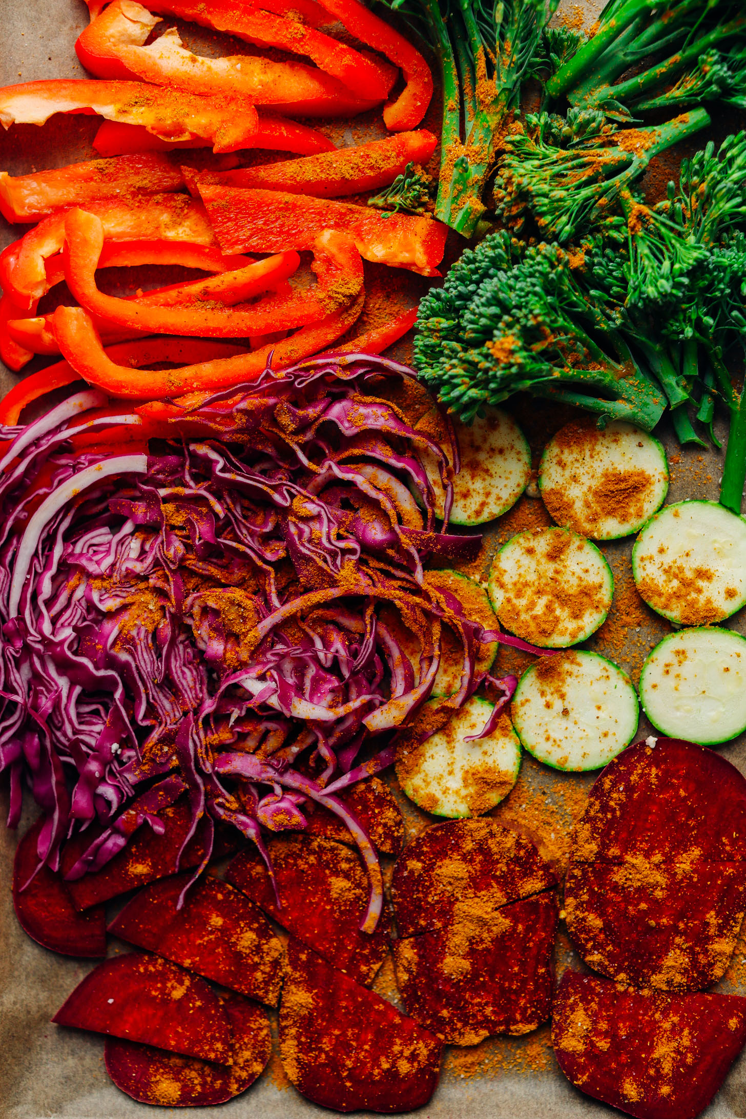 Parchment-lined baking sheet with beets, zucchini, red cabbage, broccolini, and red bell pepper for roasting