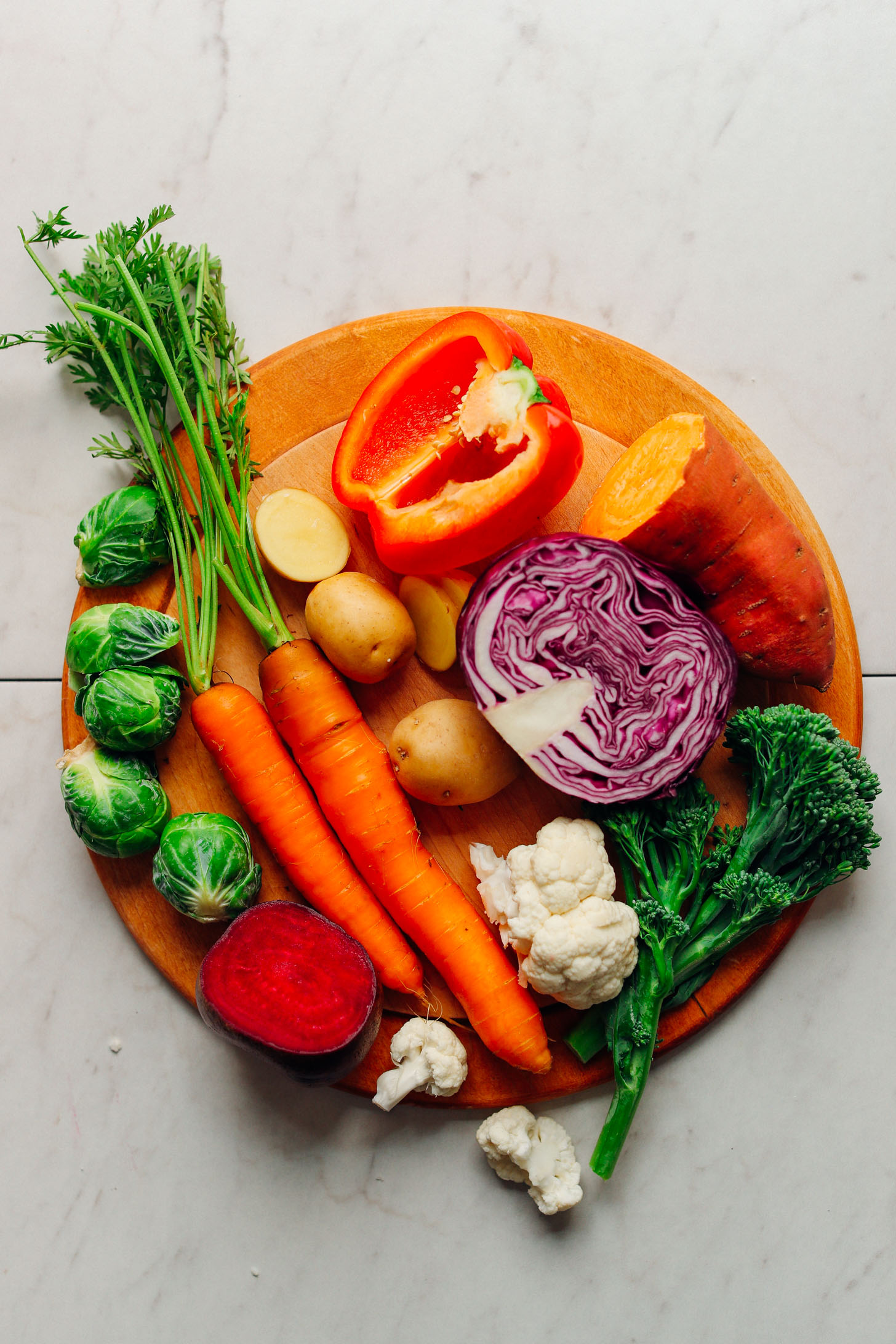 Wood cutting board with Brussels sprouts, carrots, beet, cauliflower, broccolini, sweet potato, red cabbage, red bell pepper, and potatoes
