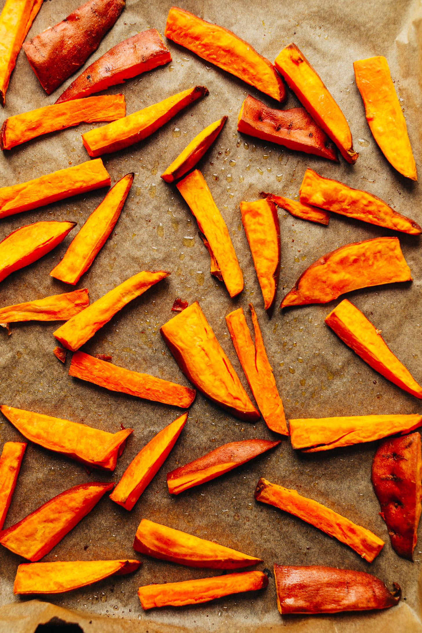 Freshly roasted sliced sweet potatoes on a parchment-lined baking sheet