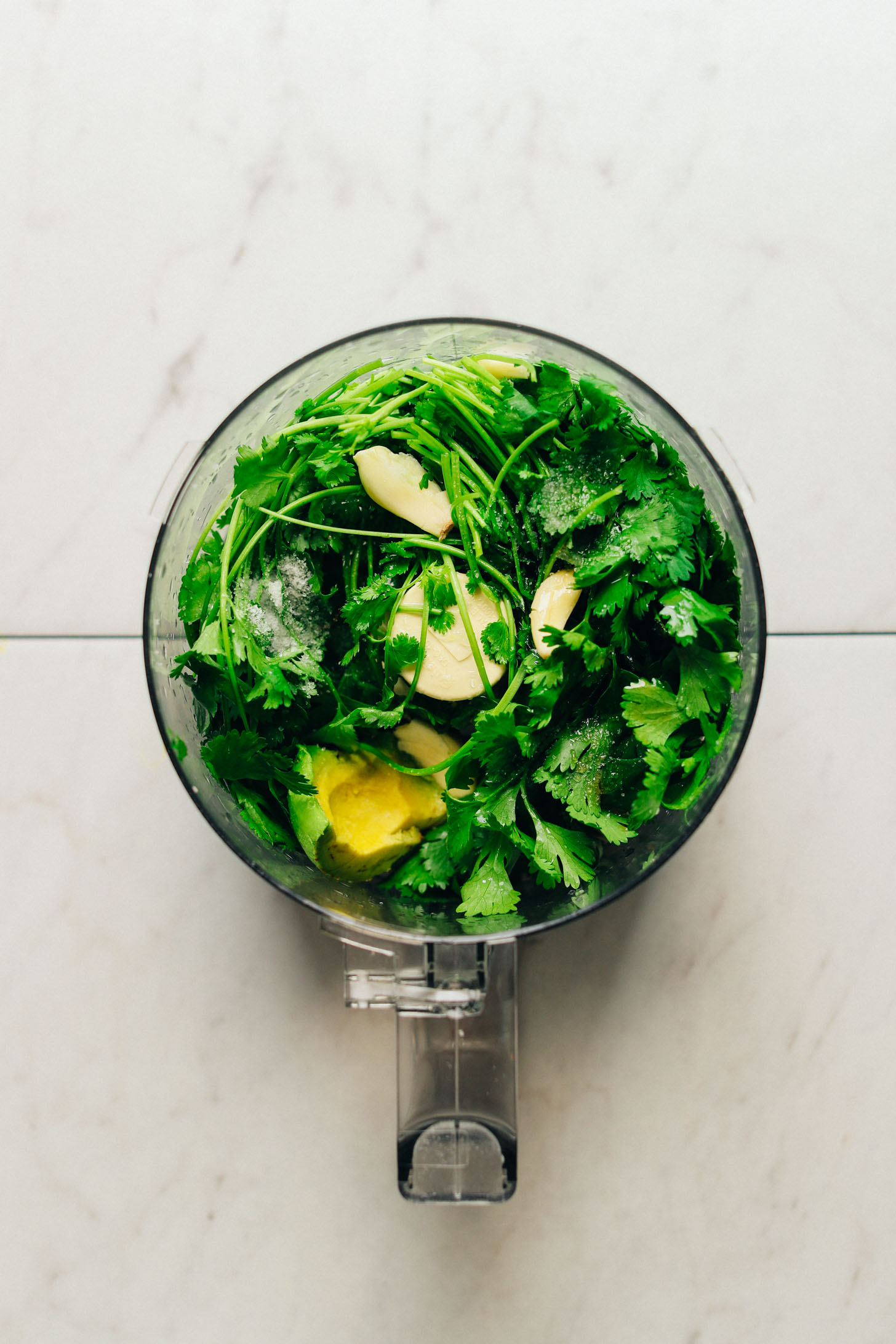 Cilantro chutney ingredients in a food processor against a white marble background