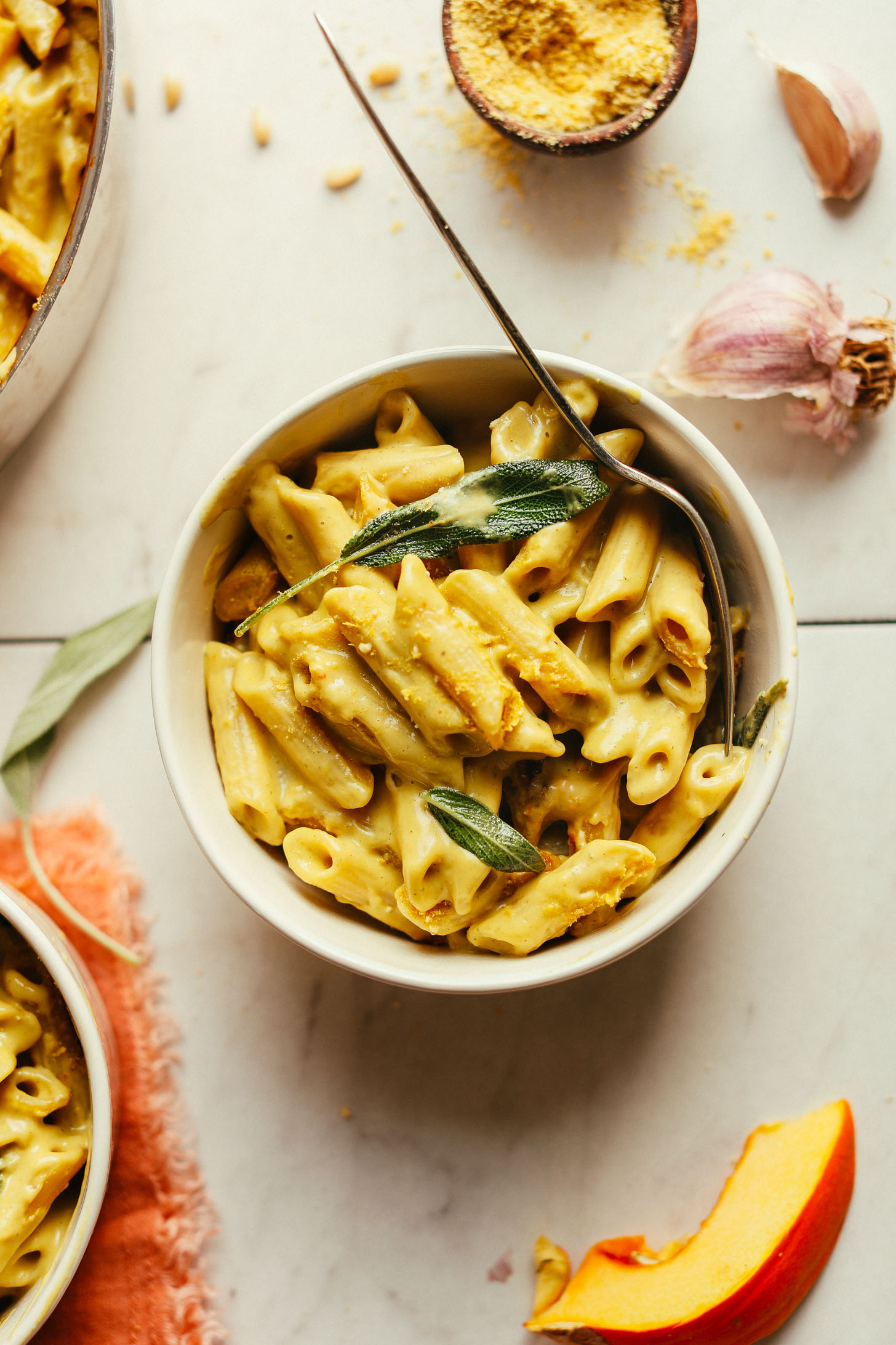 Bowl of comforting gluten-free vegan Pumpkin Mac 'n' Cheese with some vegan parmesan cheese for serving