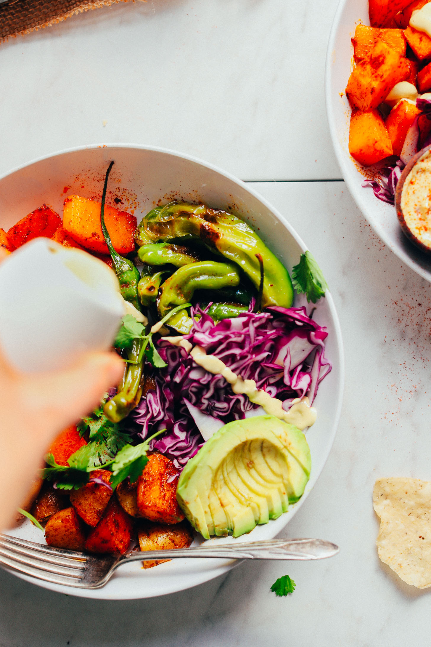 Pouring vegan queso over Roasted Butternut Squash Bowls loaded with veggies