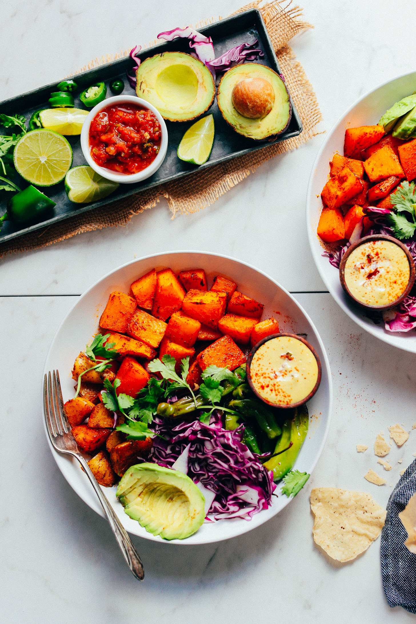 Dinner bowls filled with roasted squash, potatoes, avocado, cilantro, cabbage, peppers, and vegan quest