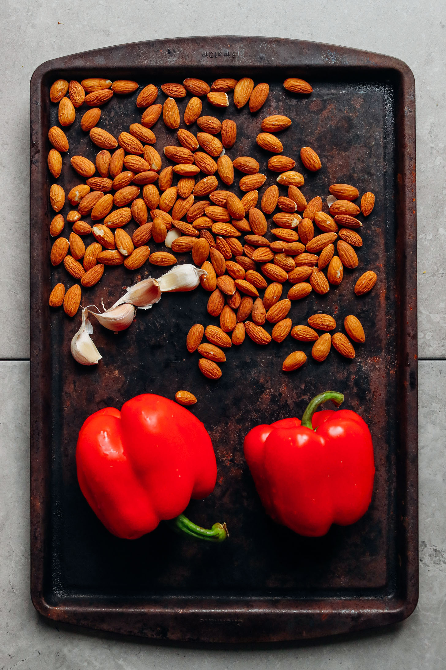 Baking sheet displaying almonds, red bell peppers, and garlic ready for roasting