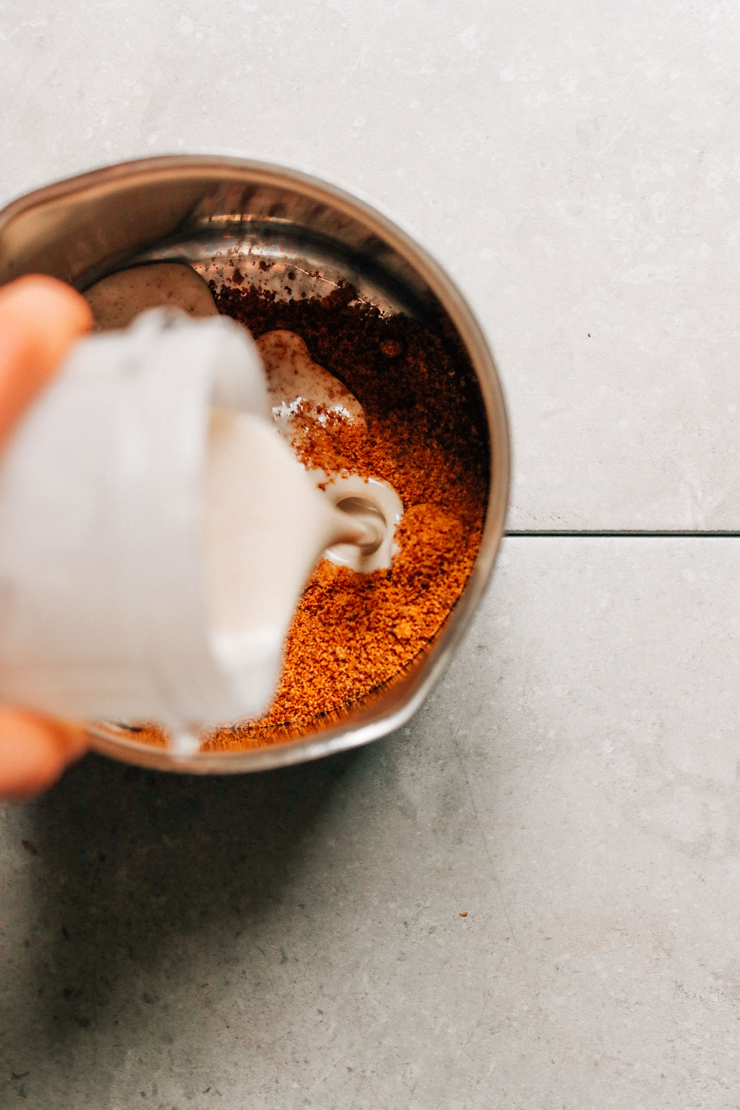Pouring coconut cream into a saucepan filled with ingredients for making plant-based Caramel Sauce