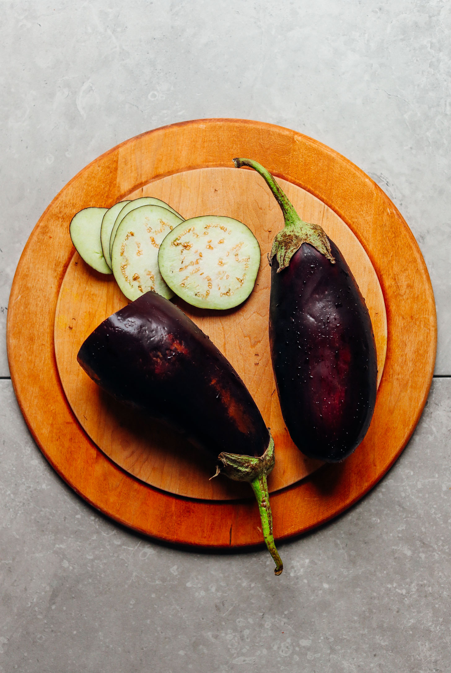 Whole and sliced eggplant on a wood cutting board